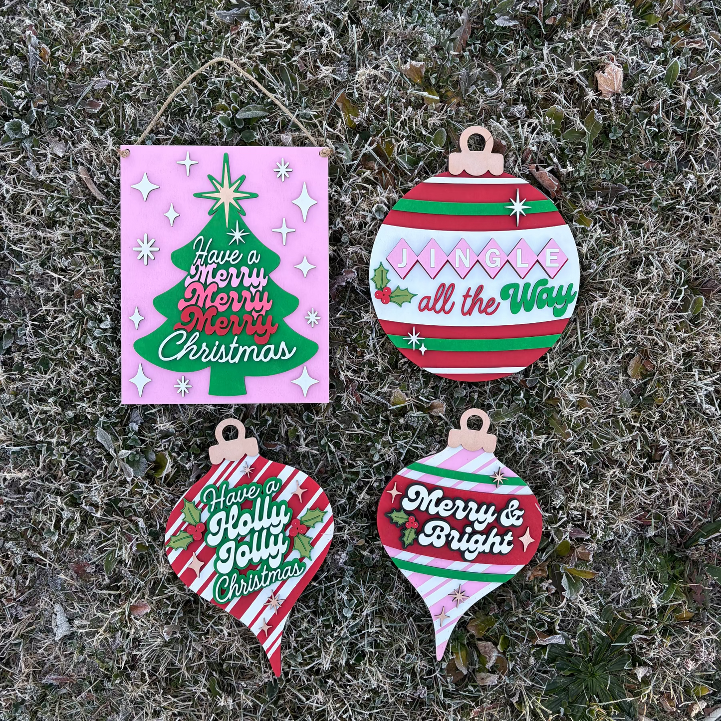 Four Christmas-themed wooden ornaments on a frosty grass background