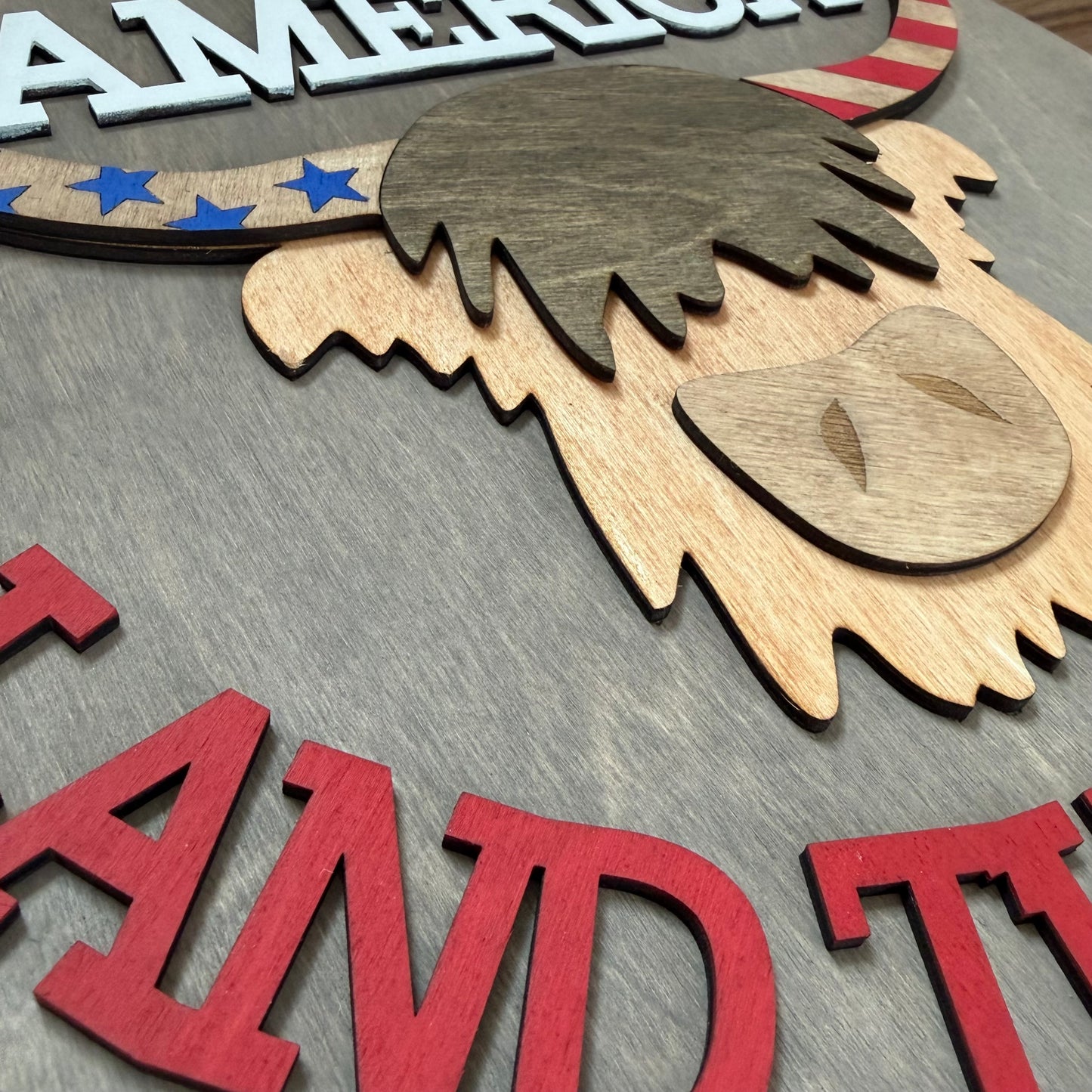Wooden 3D sign with American flag design and highland cow on a gray background