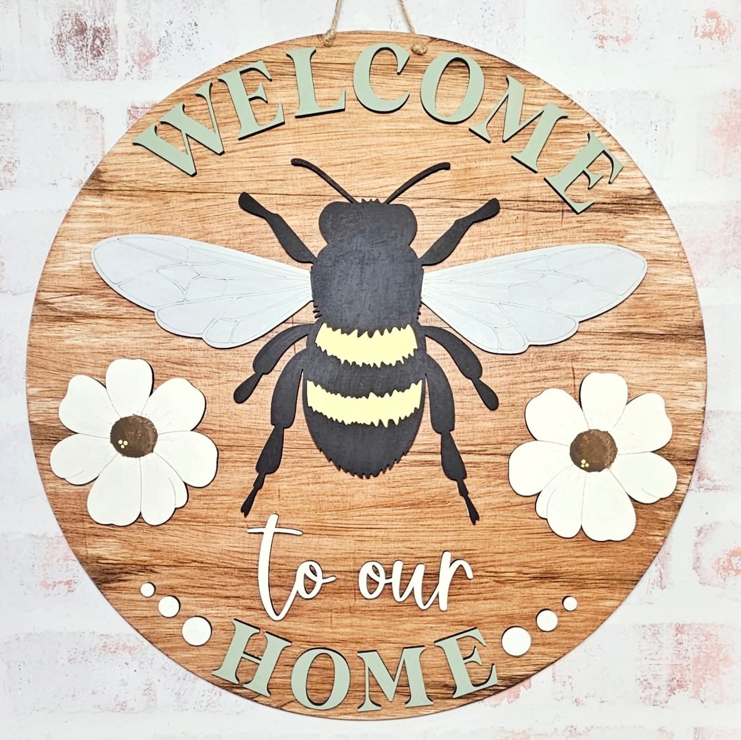 A round wooden welcome sign featuring a bumble bee design with the text 'WELCOME to our HOME' surrounded by floral accents.