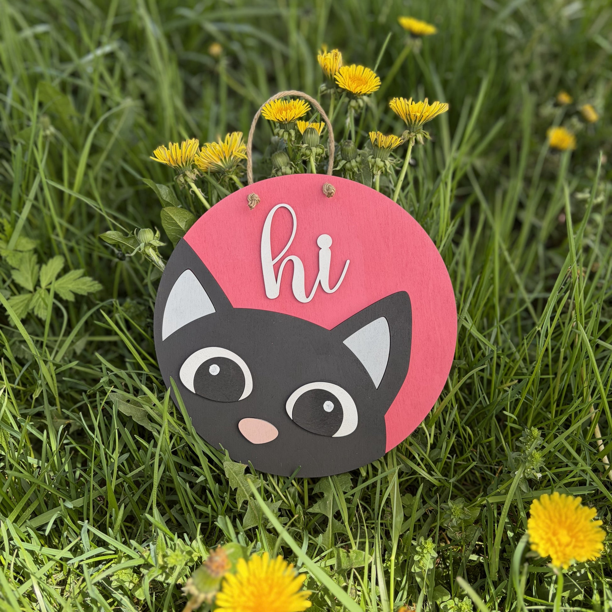 3D wood sign on the grass with a cat peeking out saying "hi"