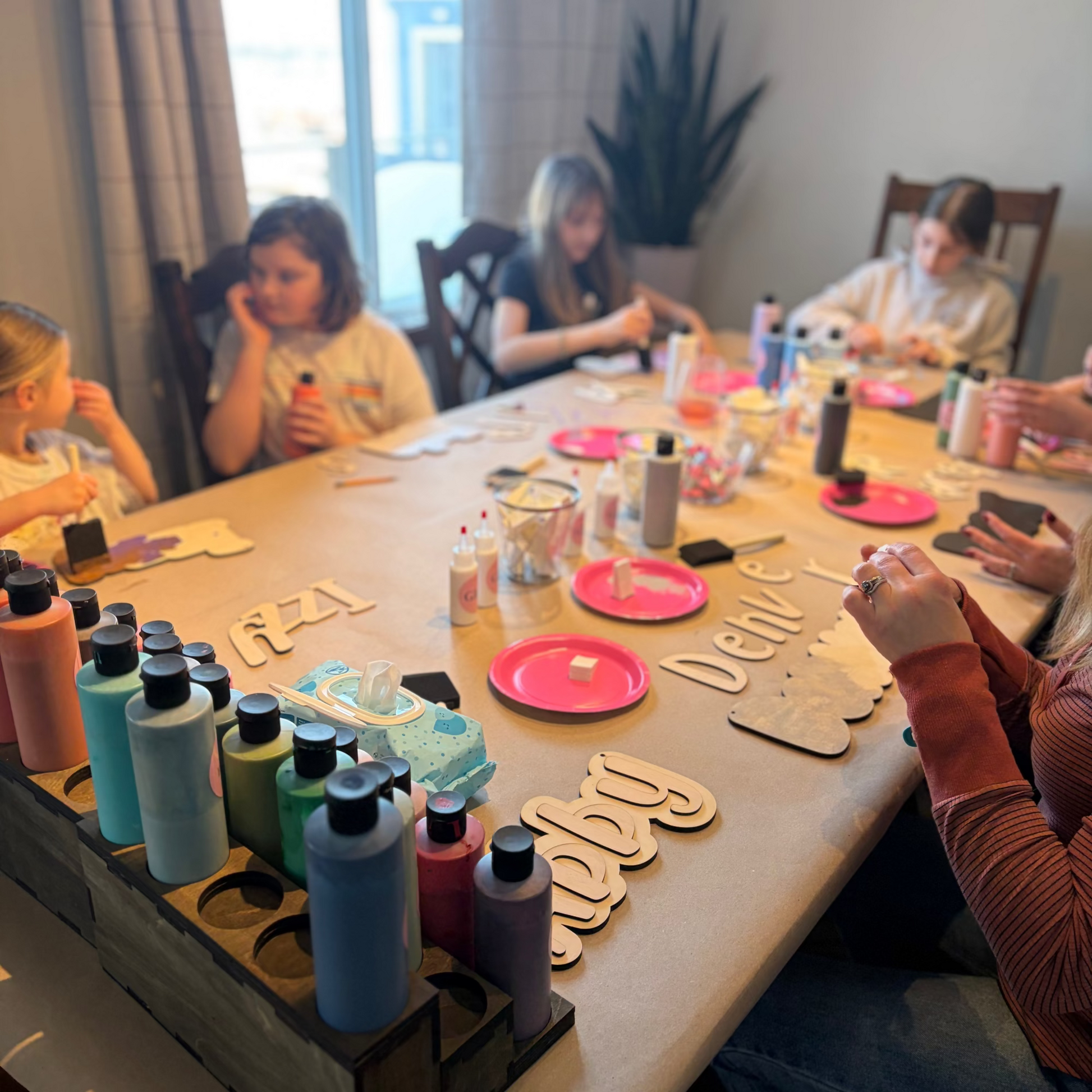 Children at a table with craft supplies and paint bottles, engaged in a creative activity.
