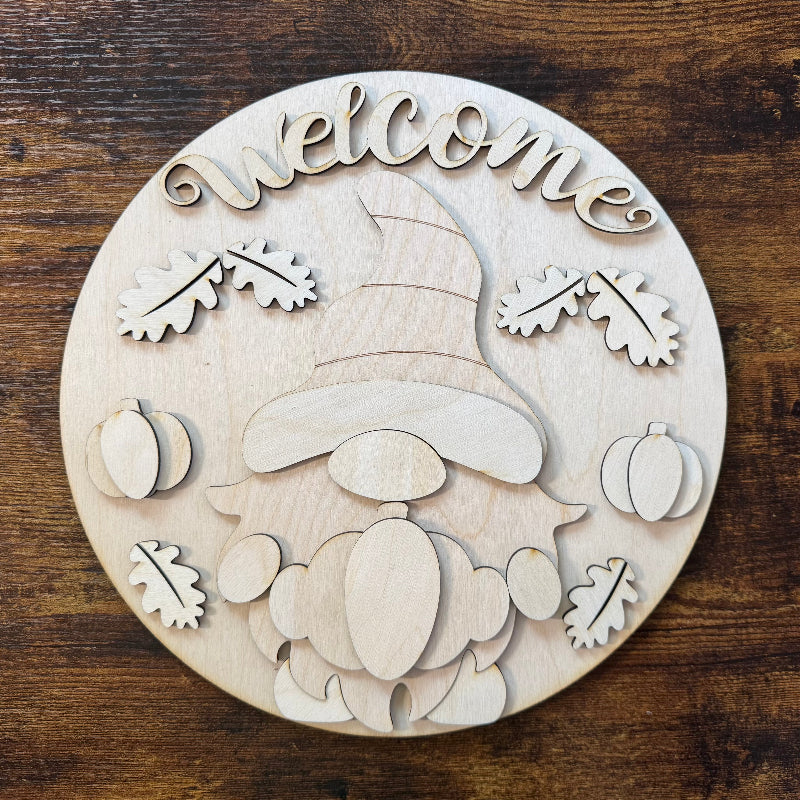 Wooden circular decoration with a gnome, pumpkins, and leaves on a wooden background