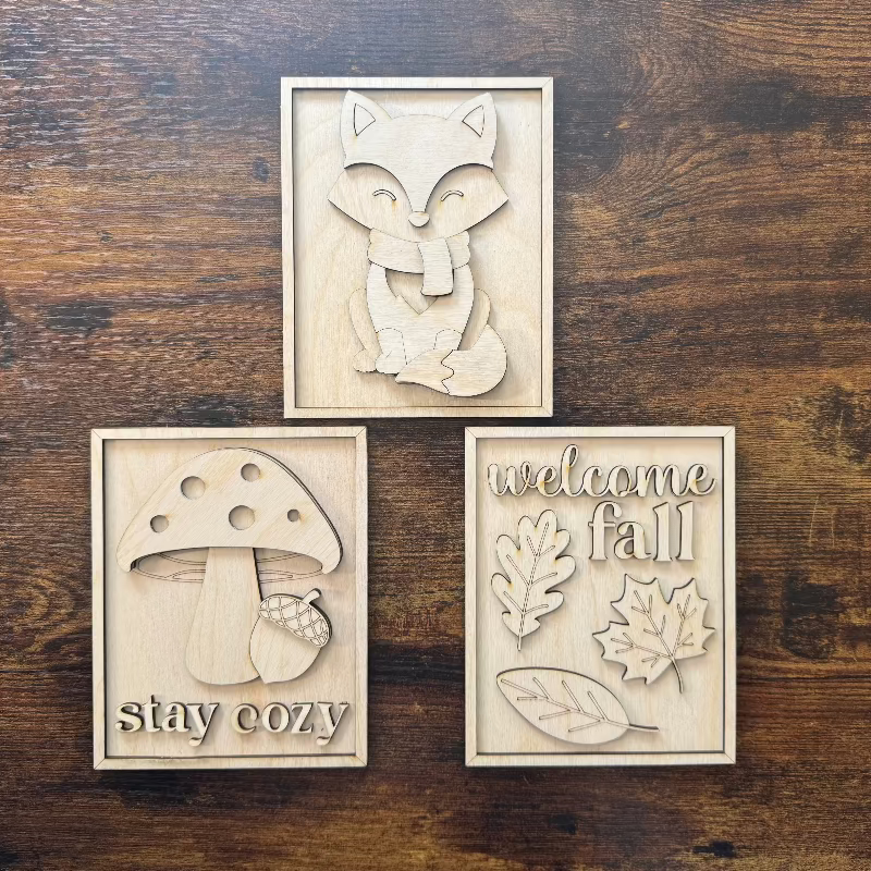 Three wooden cutouts with autumn-themed designs on a wooden surface.