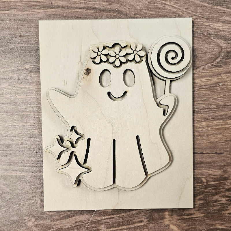 Wooden cutout of a ghost with a flower headband and lollipop on a wooden surface