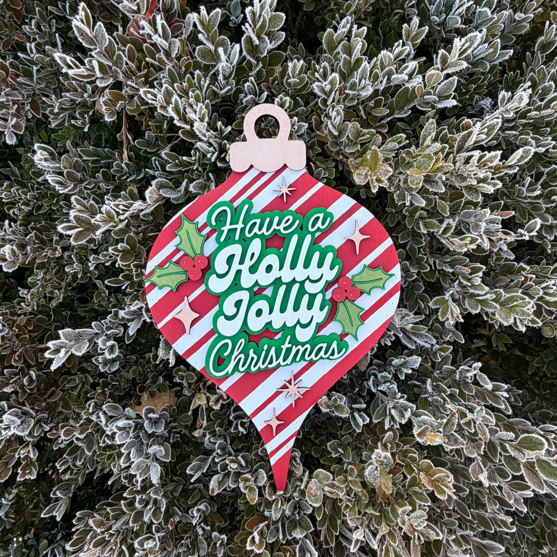 Decorative Christmas ornament sign with 'Holly Jolly Christmas' text on a frosty bush background