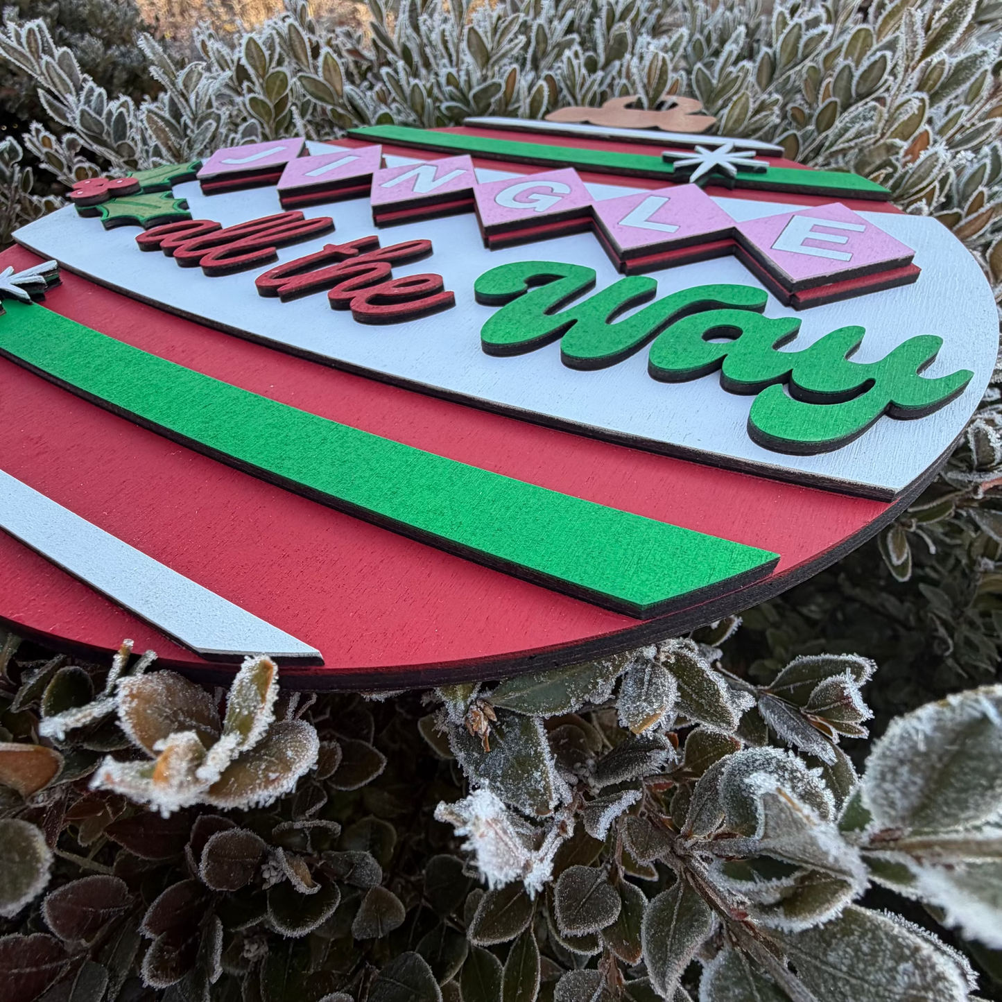 Decorative sign with 'Jingle All the Way' text on a frosty plant background