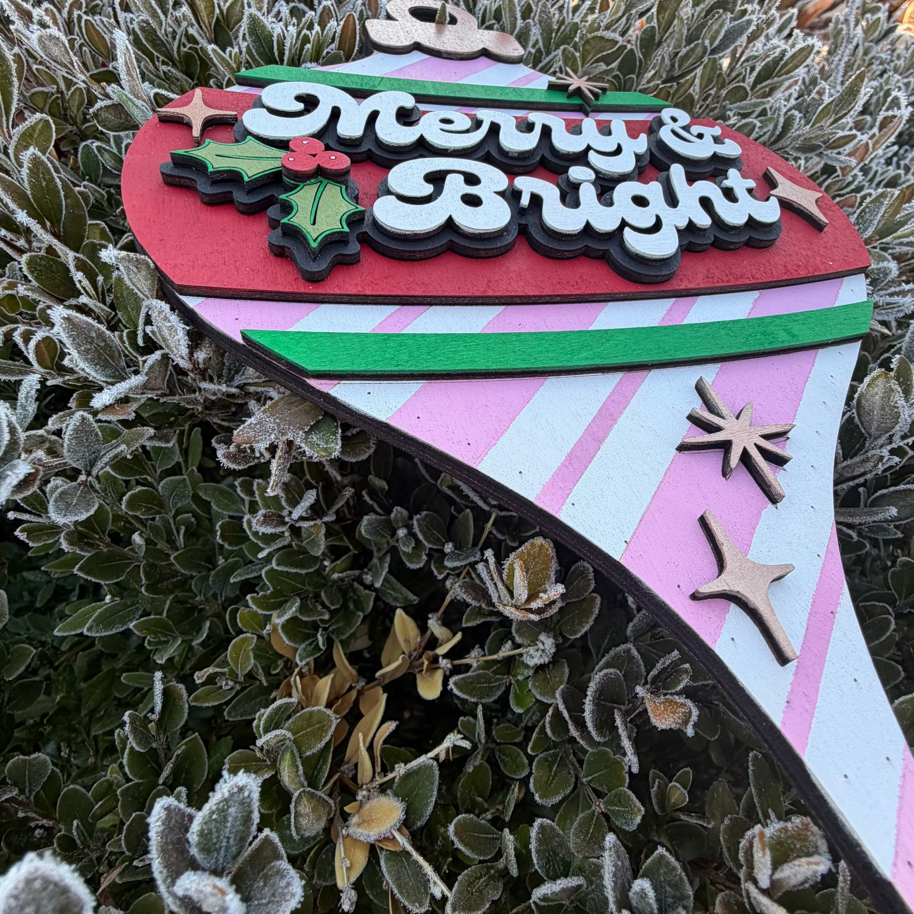 Decorative Christmas ornament with 'Merry & Bright' text on a striped background, hanging on a frosted branch.