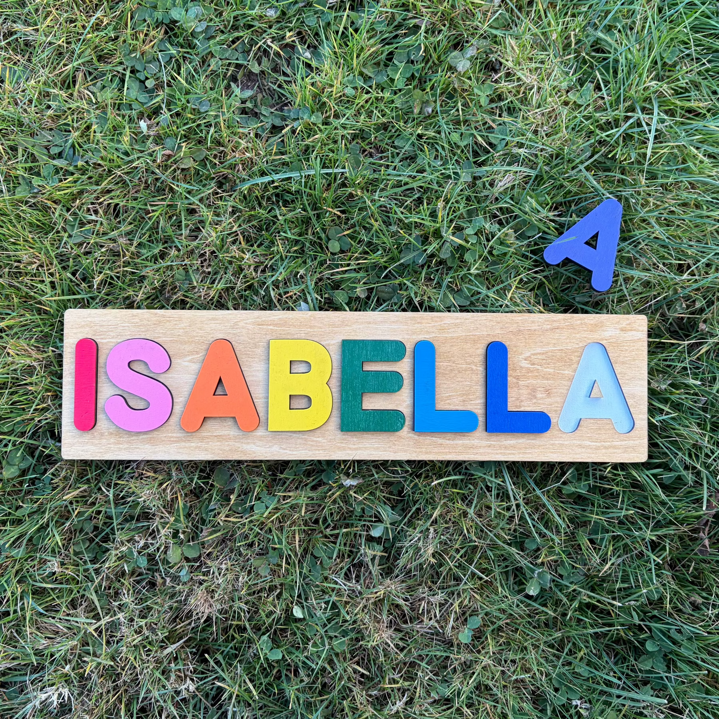 Colorful wooden puzzle with the name 'ISABELLA' on grass