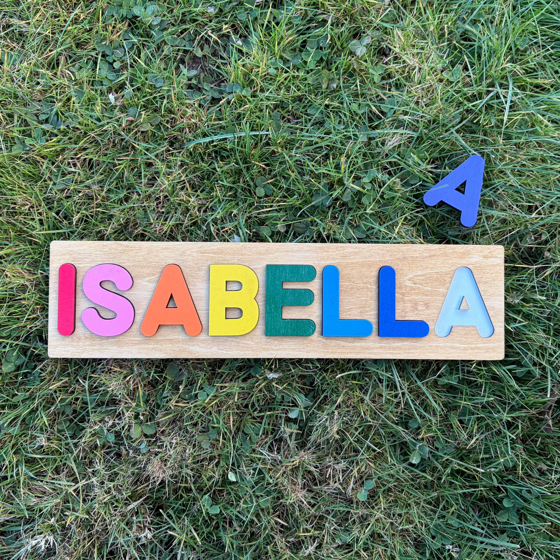 Colorful wooden puzzle with the name 'ISABELLA' on grass