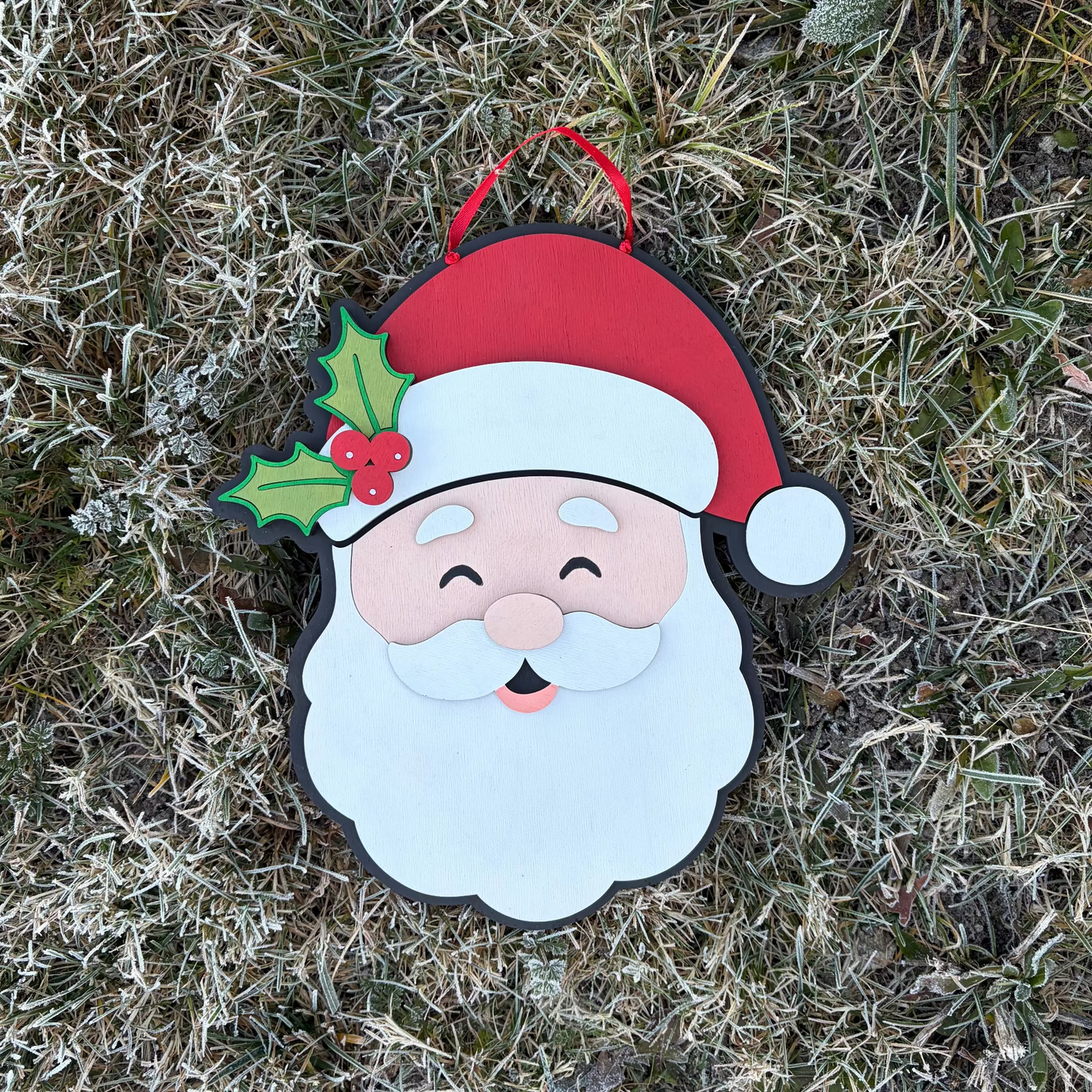 Decorative 3D Wood Santa Claus door hanger with a red hat and holly leaf on a frosty bush background