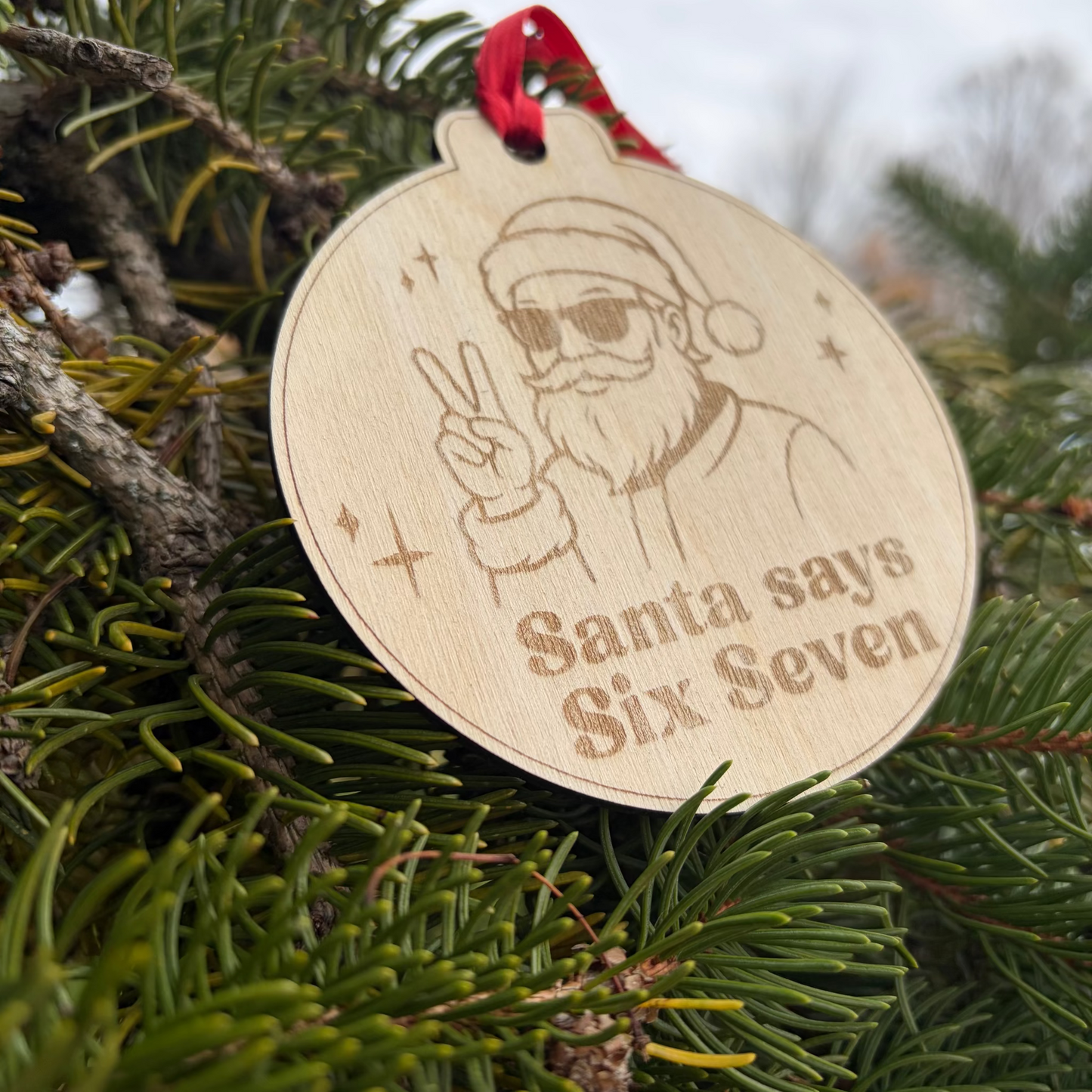 Wooden ornament with a design of Santa Claus and text 'Santa says Six Seven' hanging on a Christmas tree.