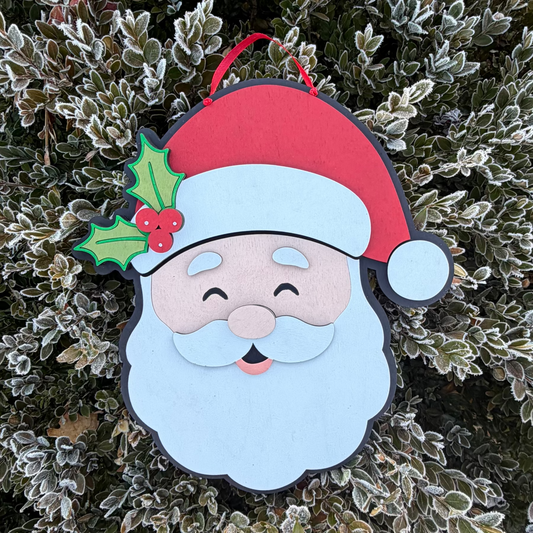 Decorative 3D Wood Santa Claus door hanger with a red hat and holly leaf on a frosty bush background
