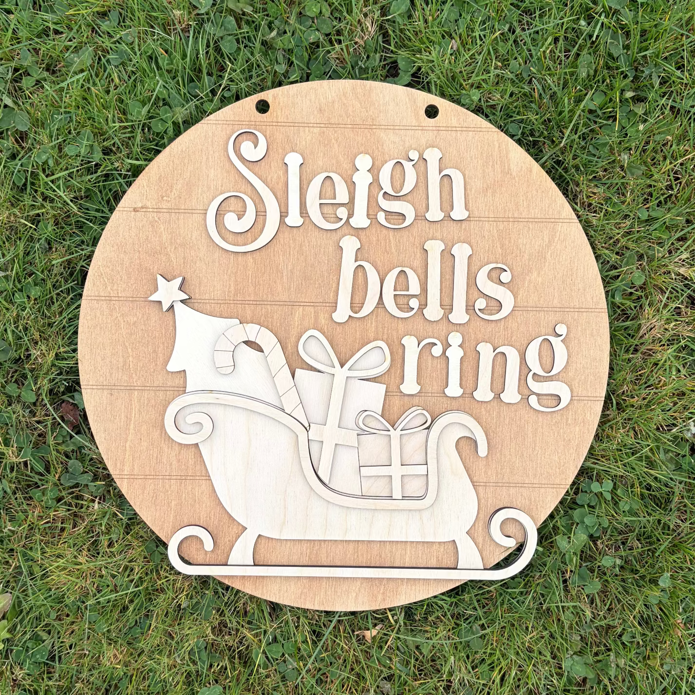 Wooden circular sign with 'Sleigh bells ring' text and Santa sleigh design on grass