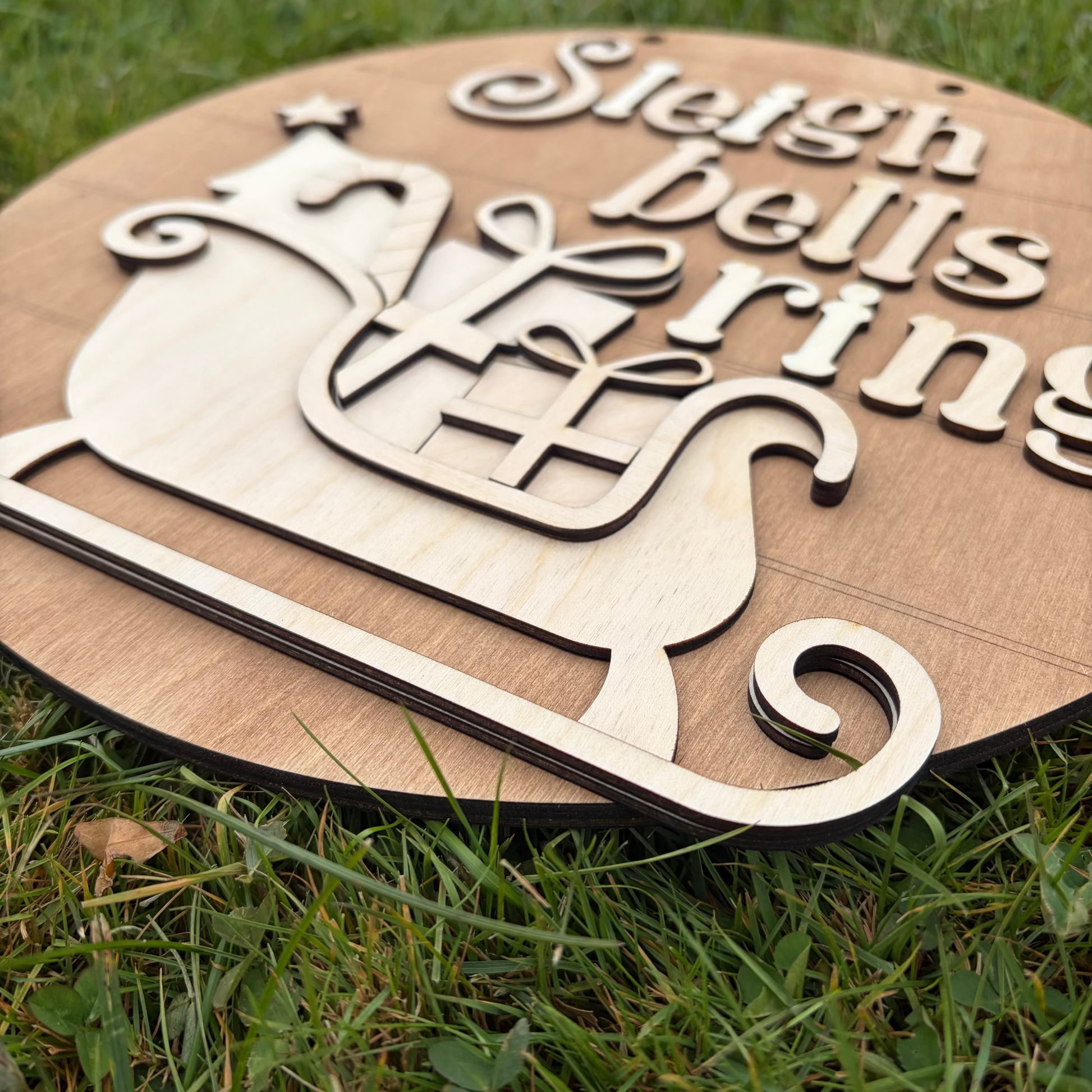 Wooden sign with 'Sleigh bells ring' text and reindeer design on grass