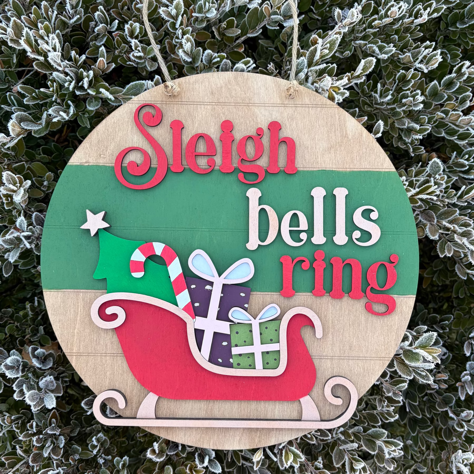 Round wooden door sign with 'Sleigh bells ring' text and Christmas elements on a frosty background.