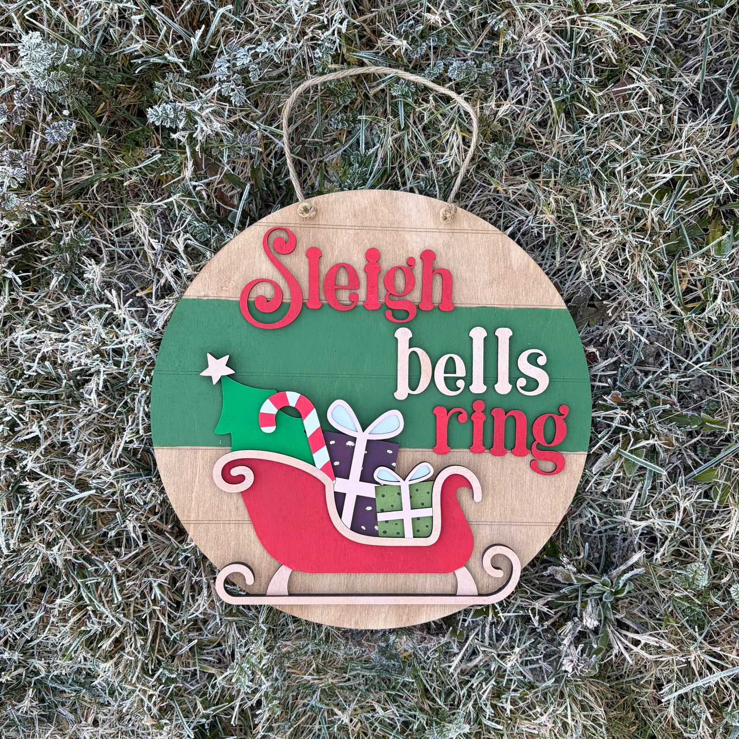 Christmas-themed wooden sign with 'Sleigh bells ring' text on a frosty grass background
