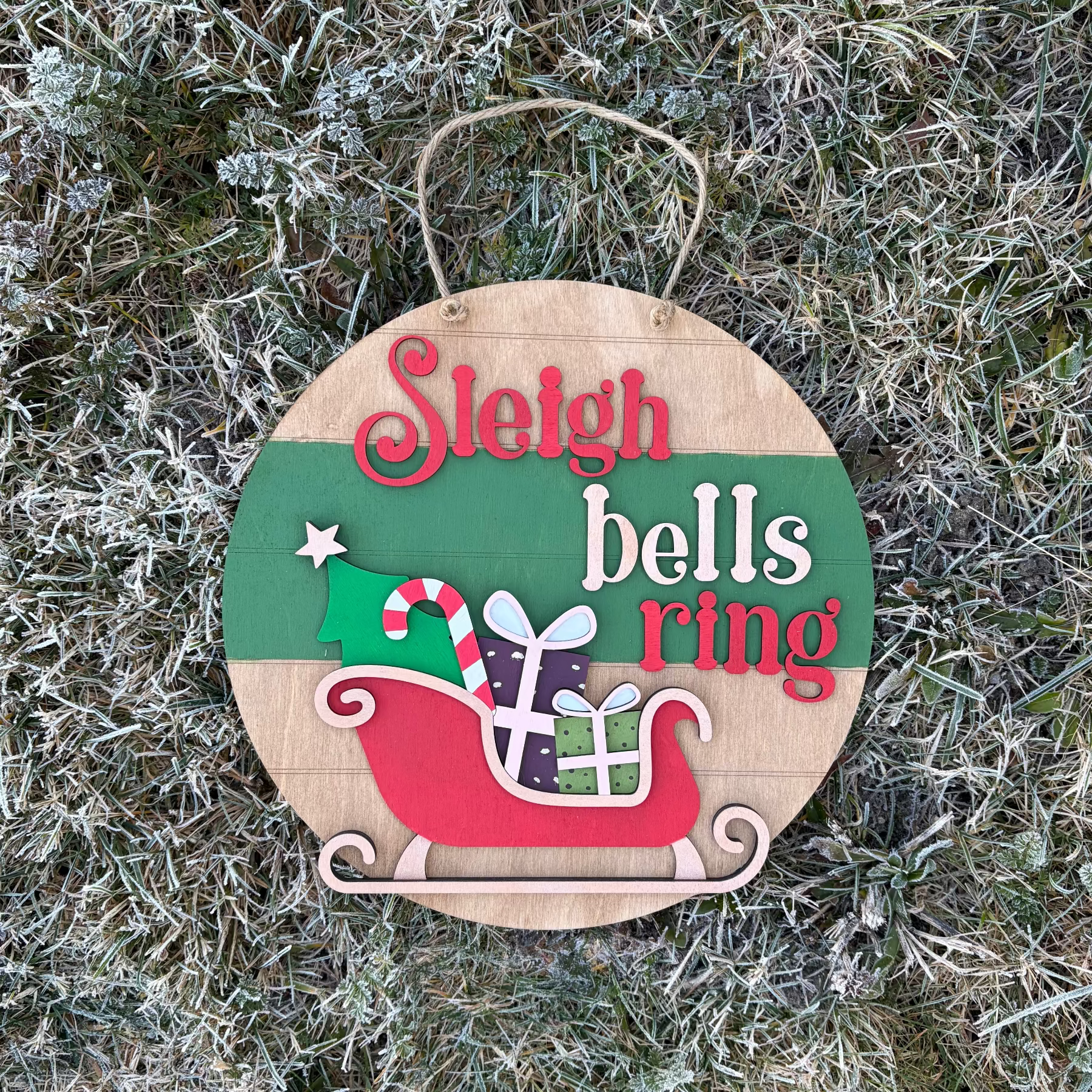 Christmas-themed wooden sign with 'Sleigh bells ring' text on a frosty grass background