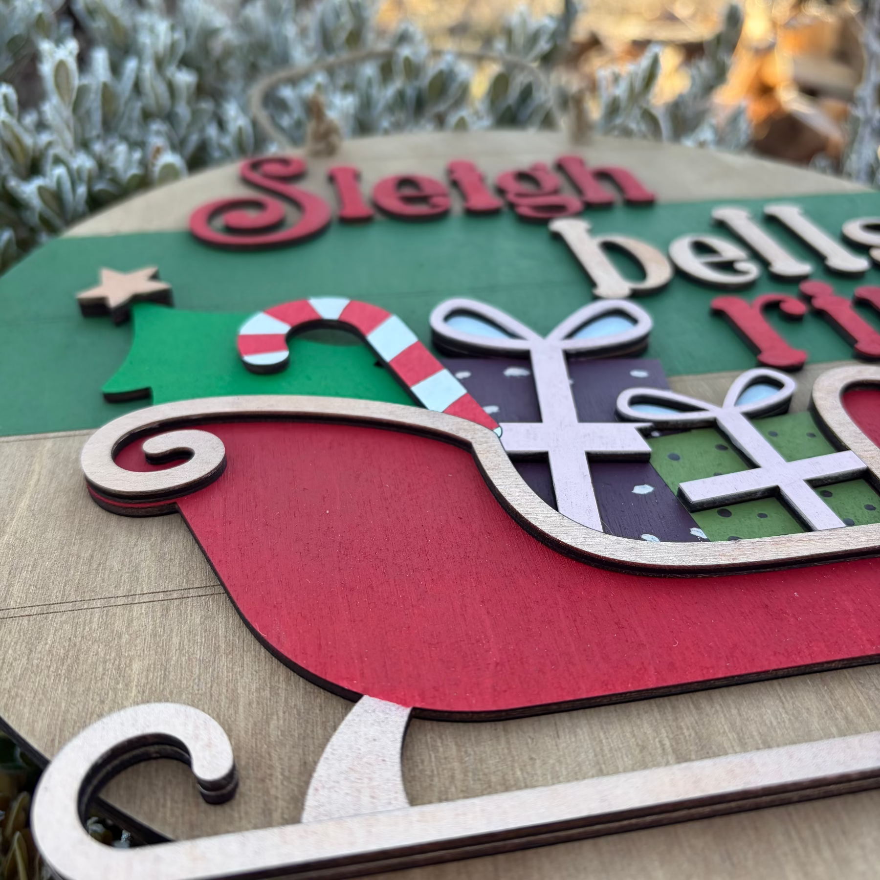Decorative sign with 'Sleigh bells ring' text and Christmas-themed elements on a wooden surface.