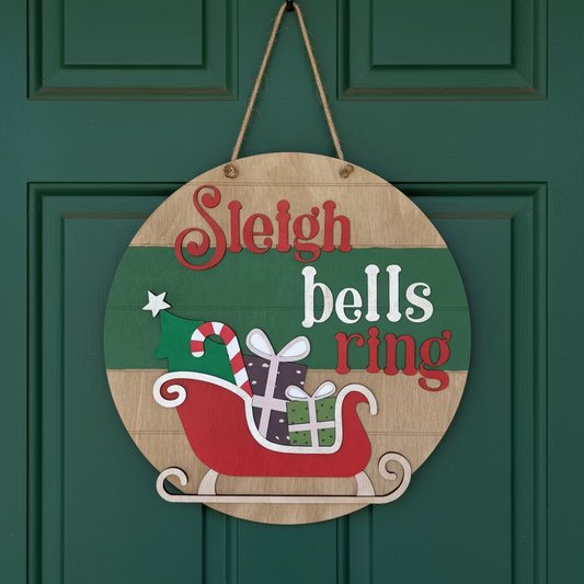 Round wooden Christmas decoration with 'Sleigh bells ring' text and a sleigh design on a wooden background.
