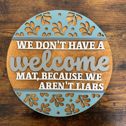 A round decorative plaque with a humorous welcome message in the center, surrounded by a blue floral pattern.