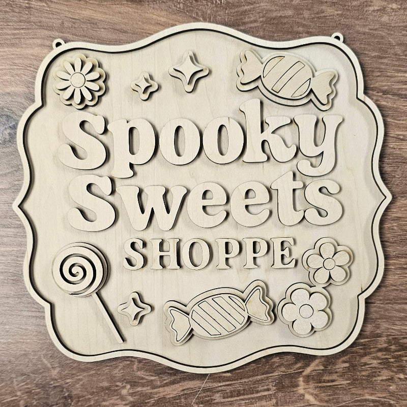 Decorative sign with 'Spooky Sweets Shoppe' text on a wooden background