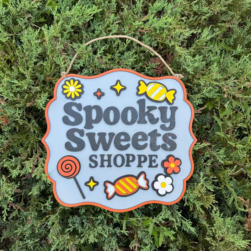 Decorative sign with 'Spooky Sweets Shoppe' text and candy graphics on a green leafy background