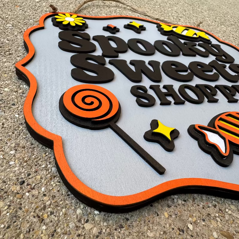 Decorative sign with 'Spooky Sweet Shop' text and Halloween-themed graphics on a concrete surface.