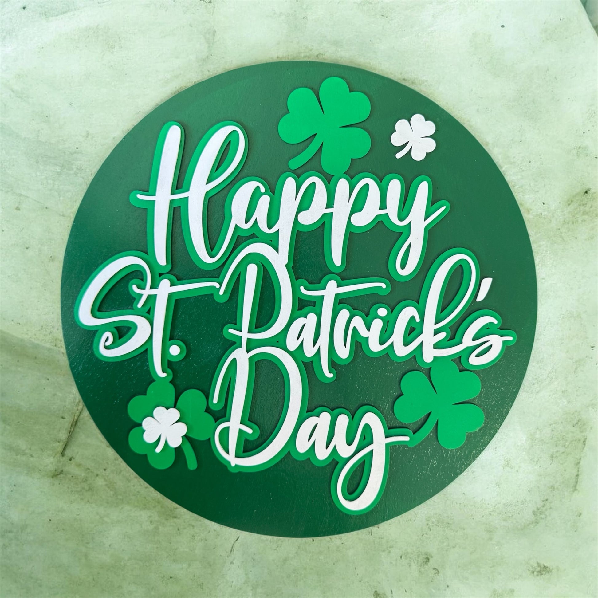 Round green sign with 'Happy St. Patrick's Day' text and shamrocks on a textured surface.