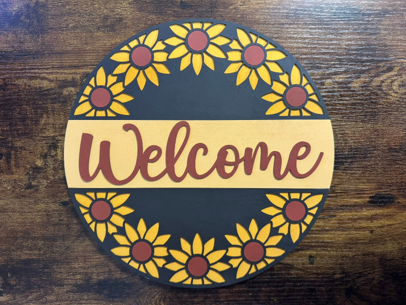 A round wooden sign with a sunflower pattern and the word 'Welcome' in the center.