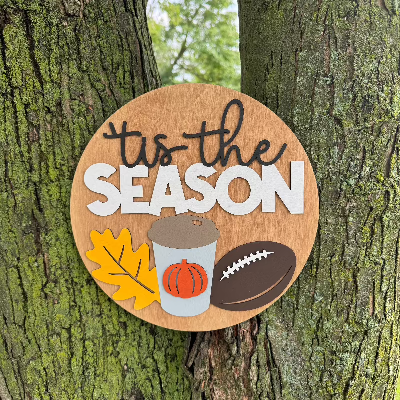 Wooden sign saying "'Tis the Season" featuring a fall leaf, coffee cup, and football.