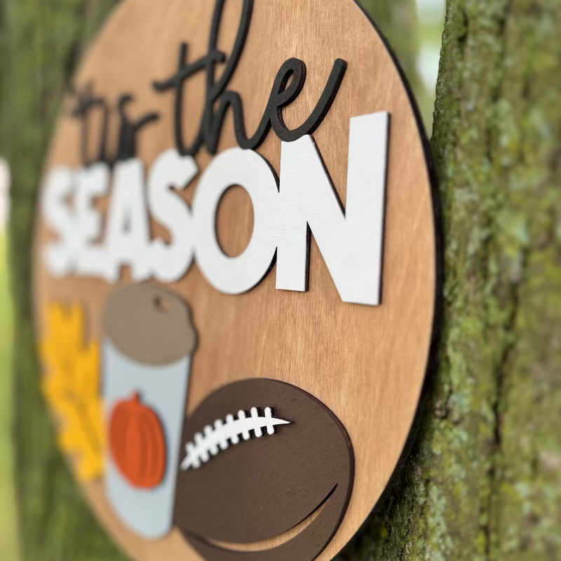 Wooden sign saying "'Tis the Season" featuring a fall leaf, coffee cup, and football.