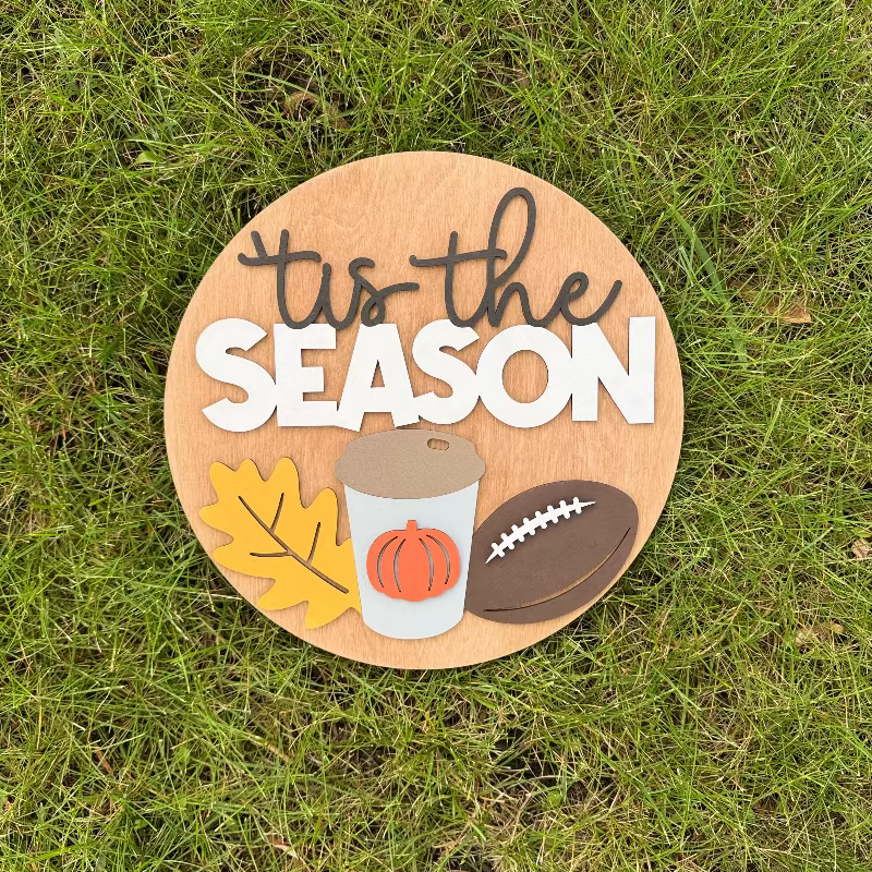Wooden sign saying "'Tis the Season" featuring a fall leaf, coffee cup, and football.