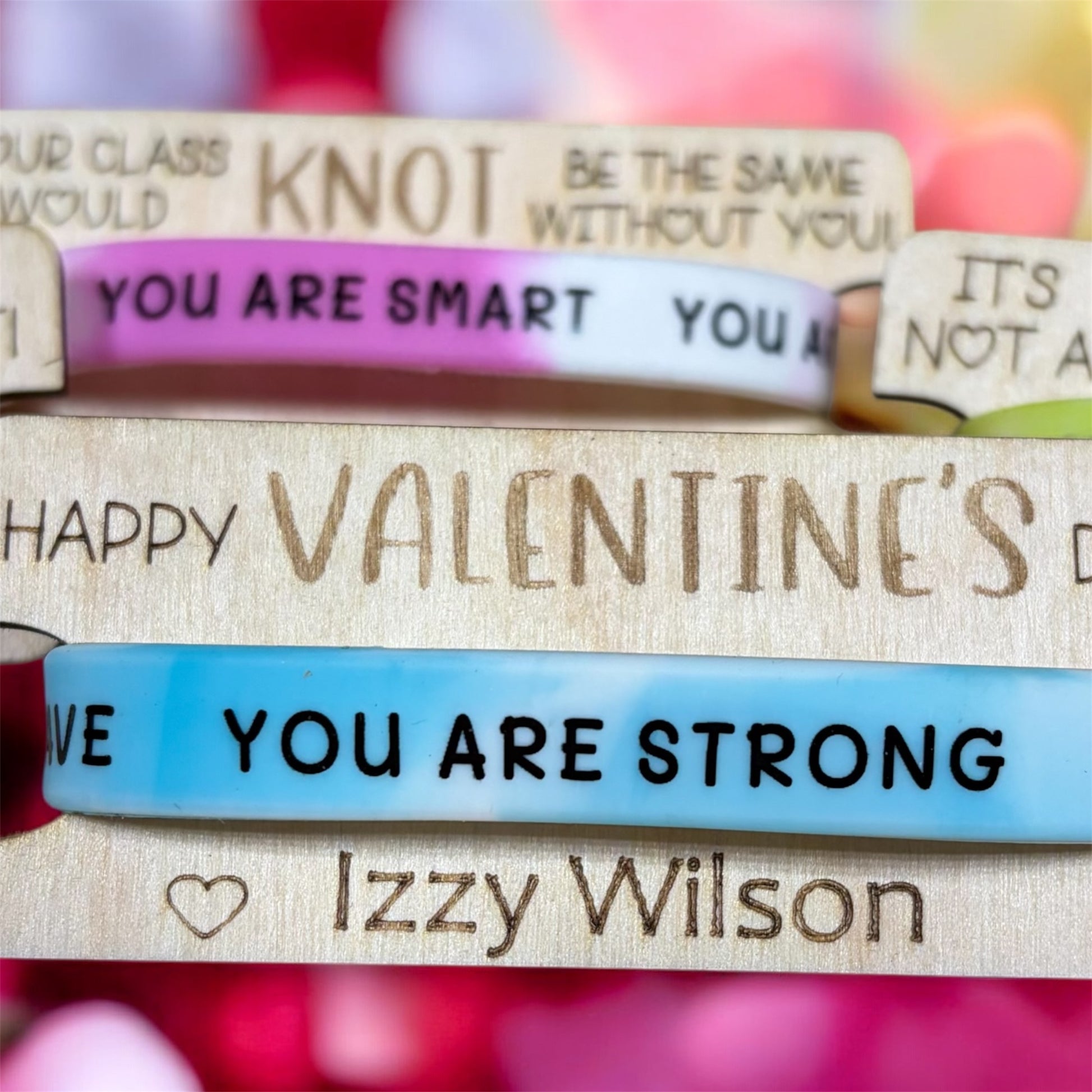Stack of wooden Valentine's Card with engraved text and colorful wristbands on a blurred background