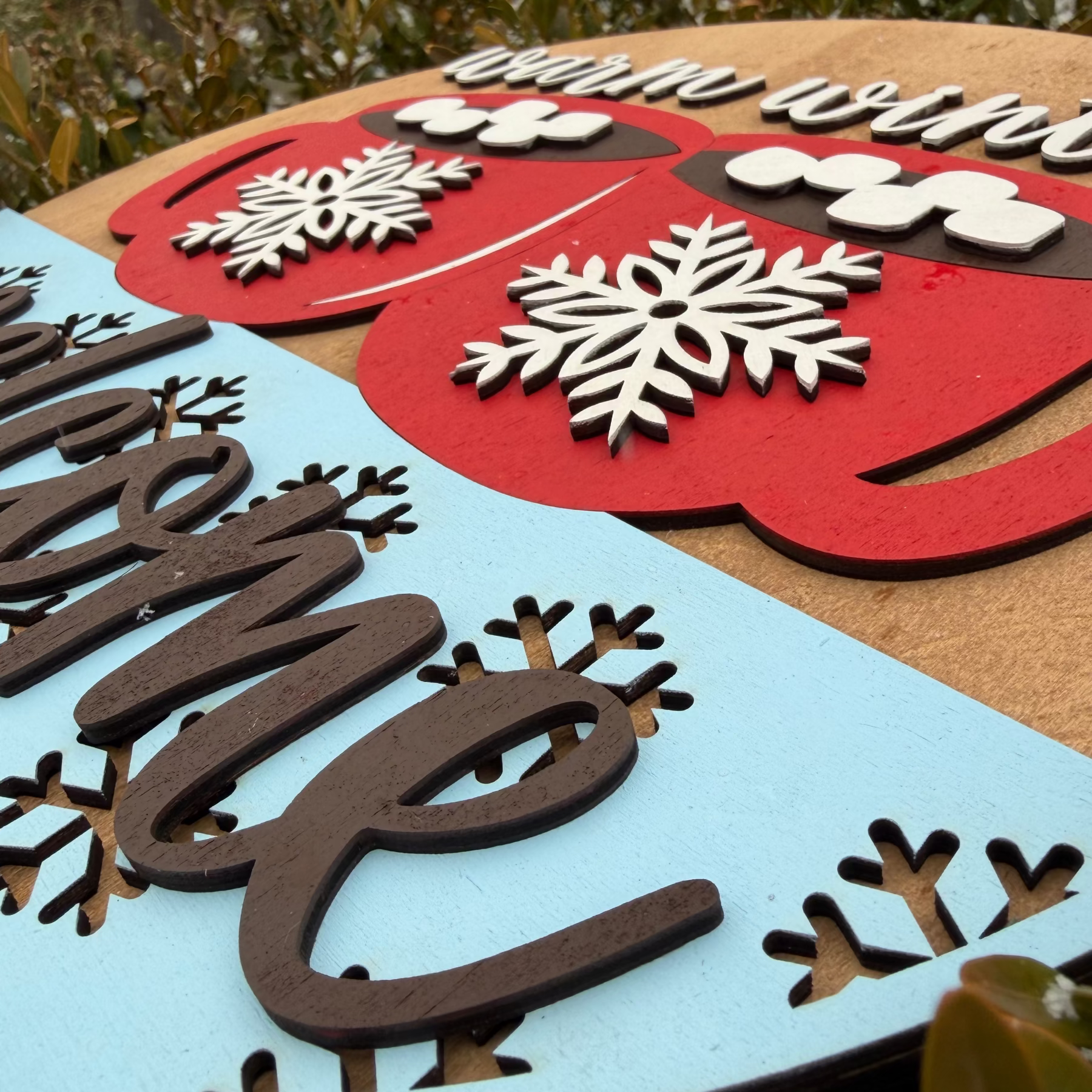 Decorative cutout letters with hot cocoa mugs and snowflakes on a wooden surface with 'Welcome' text.