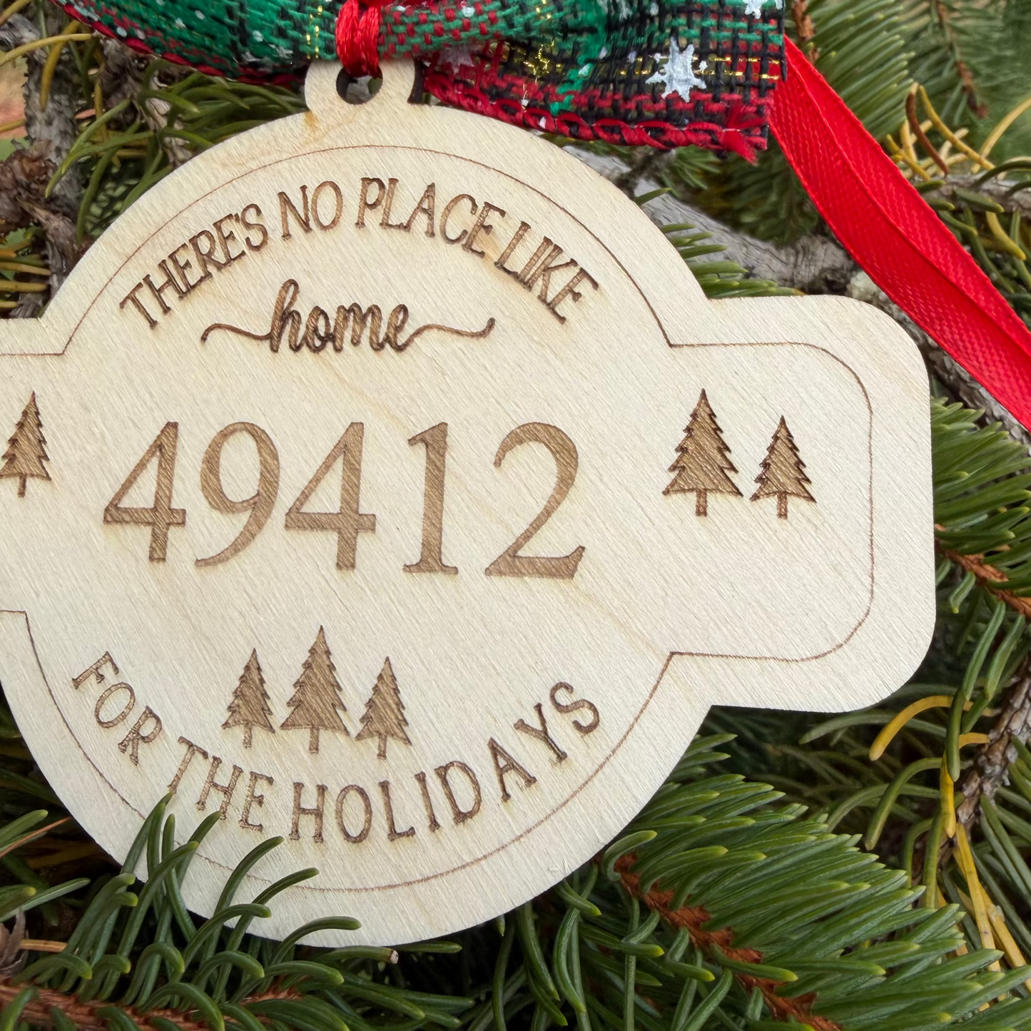 Wooden ornament with text 'THERE'S NO PLACE LIKE home 49412 FOR THE HOLIDAYS' on a Christmas tree.